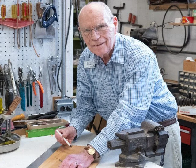 Senior man in glasses smiles and measures out wood for woodworking project at Oak Trace